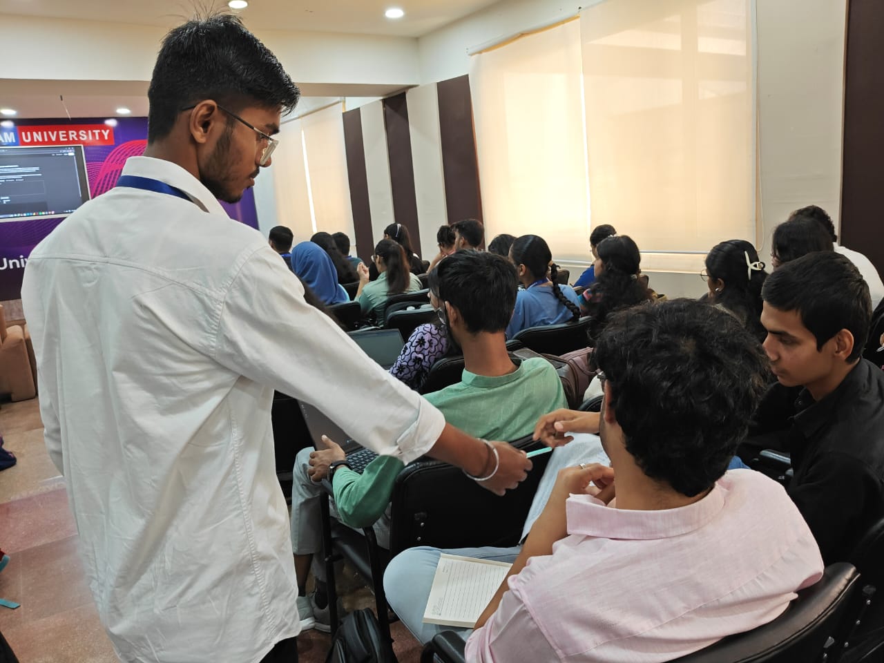 A mentor leaning over to help a seated student with their laptop during a workshop